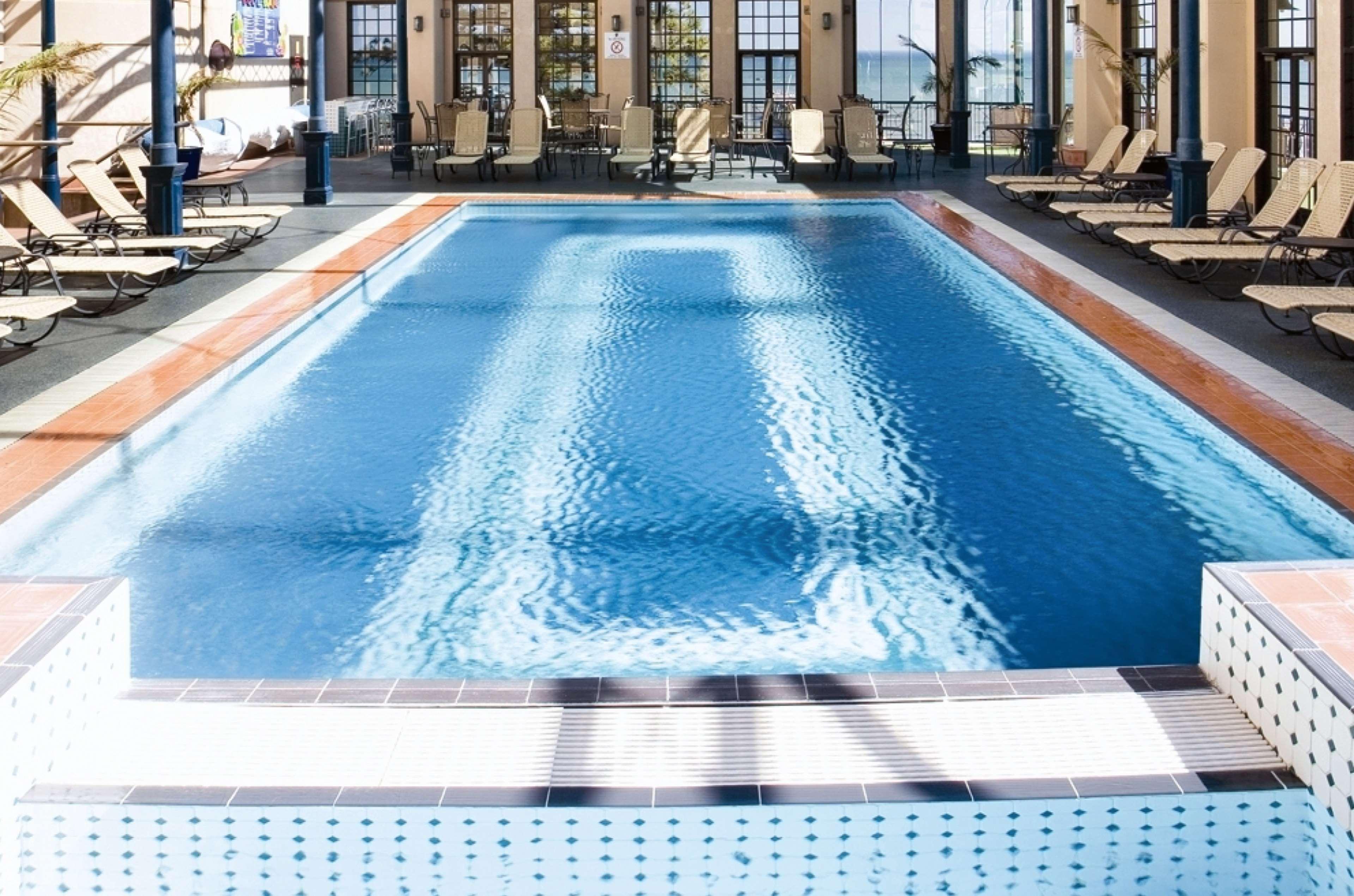Stamford Grand Adelaide Hotel Glenelg Kültér fotó The photo shows an indoor swimming pool with a pristine blue surface. The pool is surrounded by a tiled deck and has lounge chairs lined up along the sides. Large windows allow natural light to flood the area, creating a bright and inviting atmospher