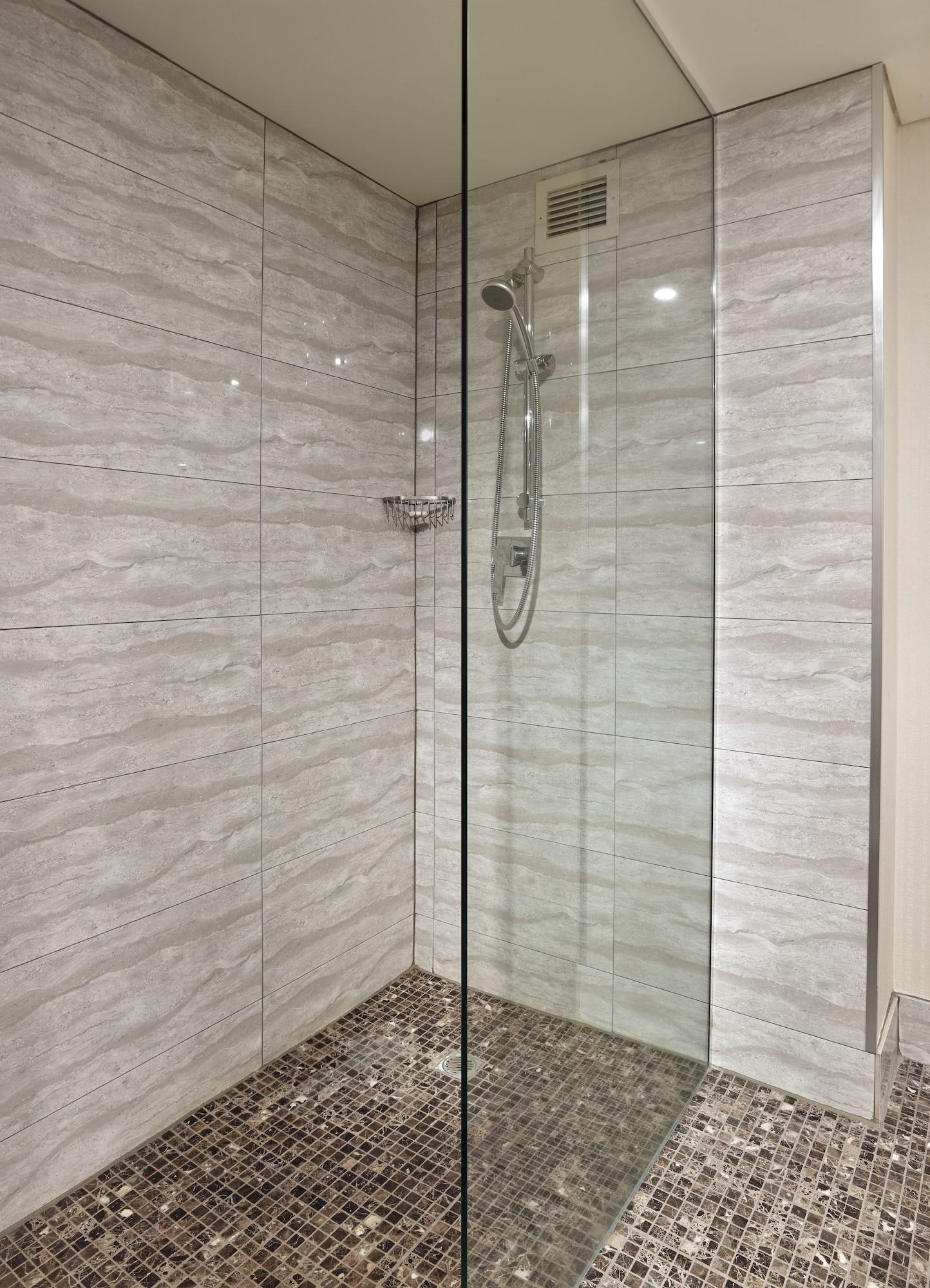 Stamford Grand Adelaide Hotel Glenelg Kültér fotó The photo shows a modern shower enclosure with a transparent glass door. The interior features tiled walls in a light, marble-like pattern, creating a clean and sleek look. There is a showerhead mounted on the wall, and the floor appears to be tiled 