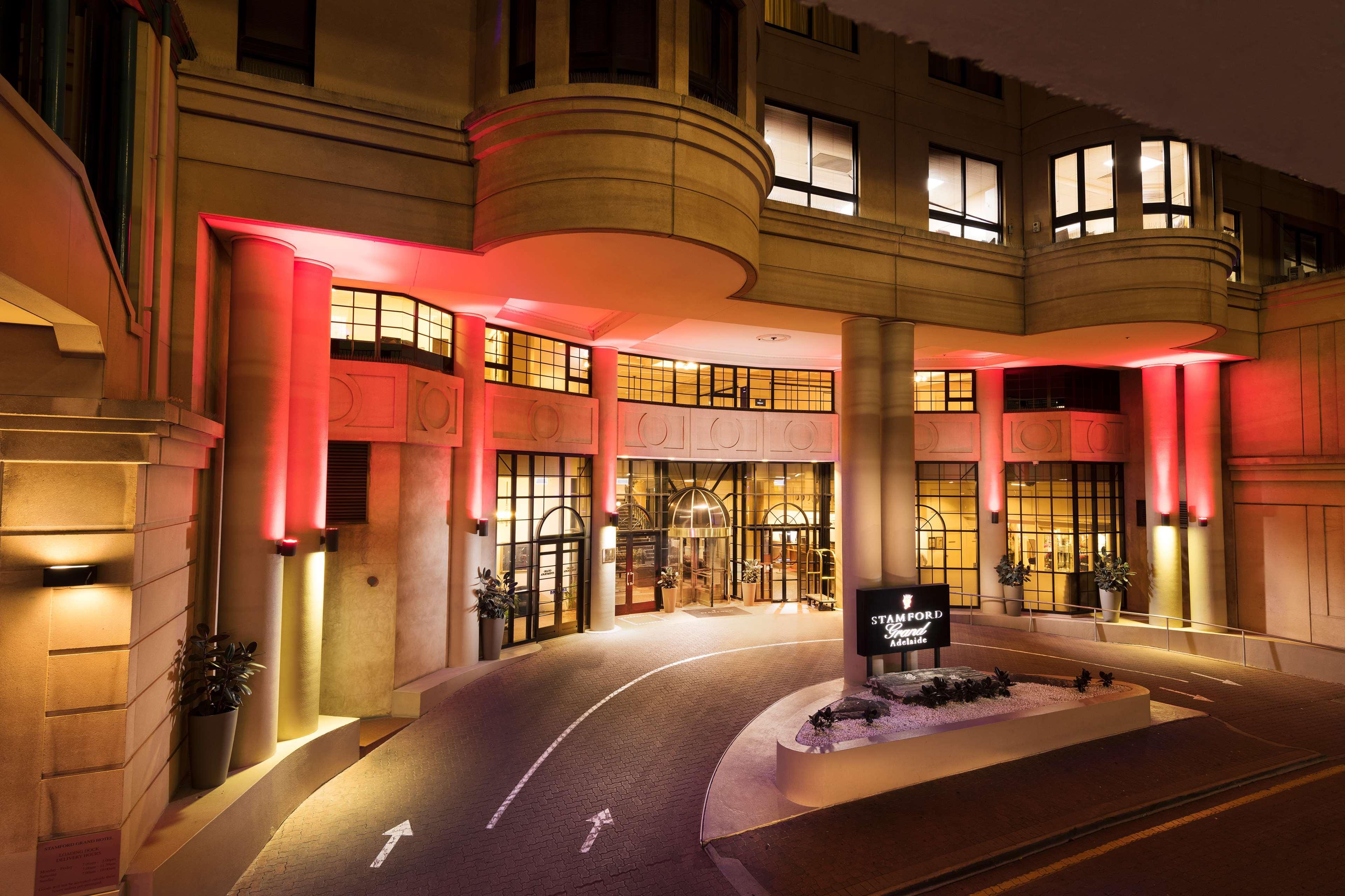 Stamford Grand Adelaide Hotel Glenelg Kültér fotó The photo shows the entrance of a hotel or luxury building at night. The façade features a modern architectural style with large windows and an elegant entrance. The area is illuminated with red lighting, creating an inviting atmosphere. There appear