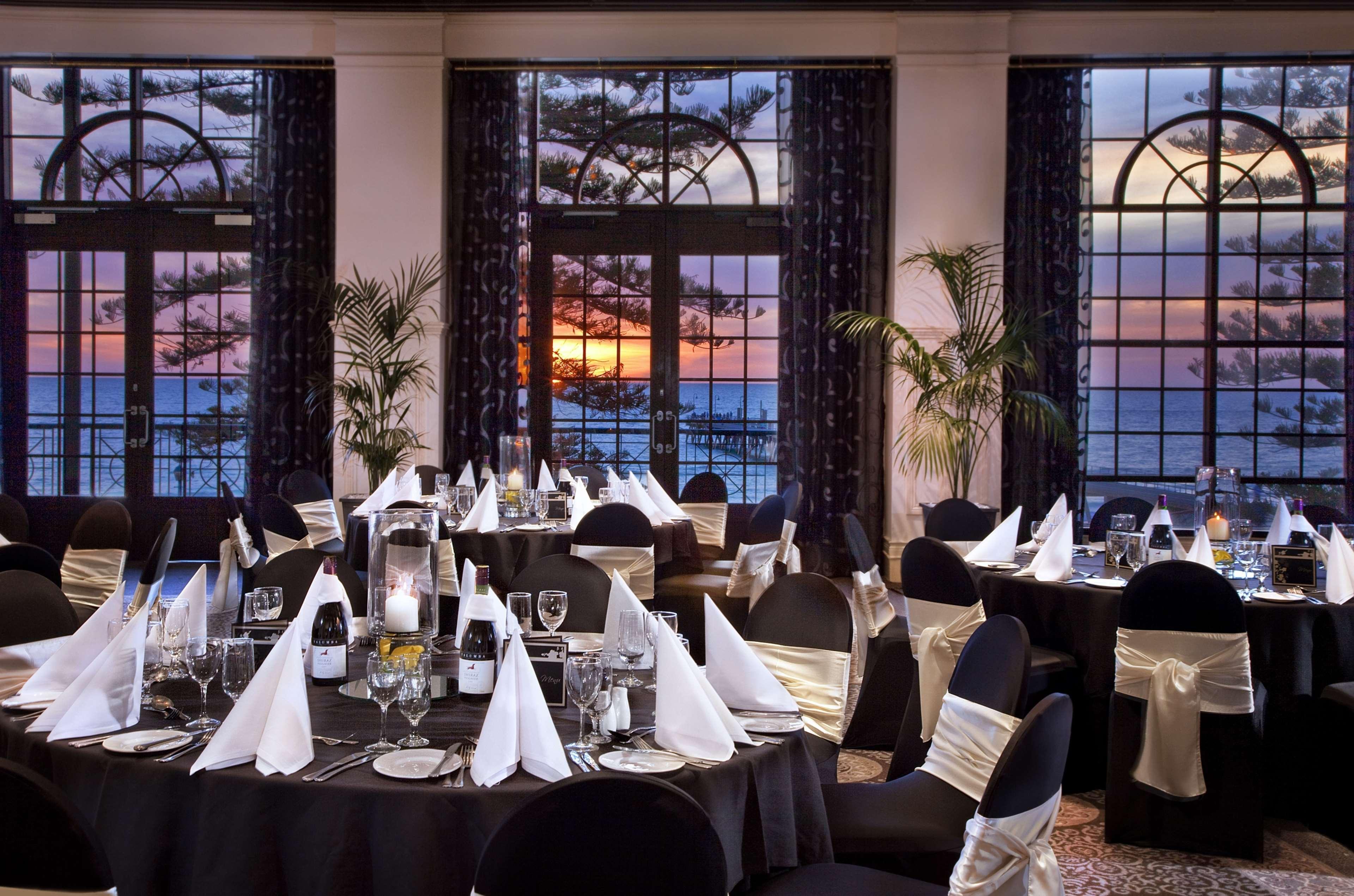 Stamford Grand Adelaide Hotel Glenelg Étterem fotó The photo shows an elegantly decorated dining room with a beautiful view. The tables are set with black tablecloths and white napkins folded in a triangular shape. There are glassware and silverware neatly arranged at each setting. The room is adorne