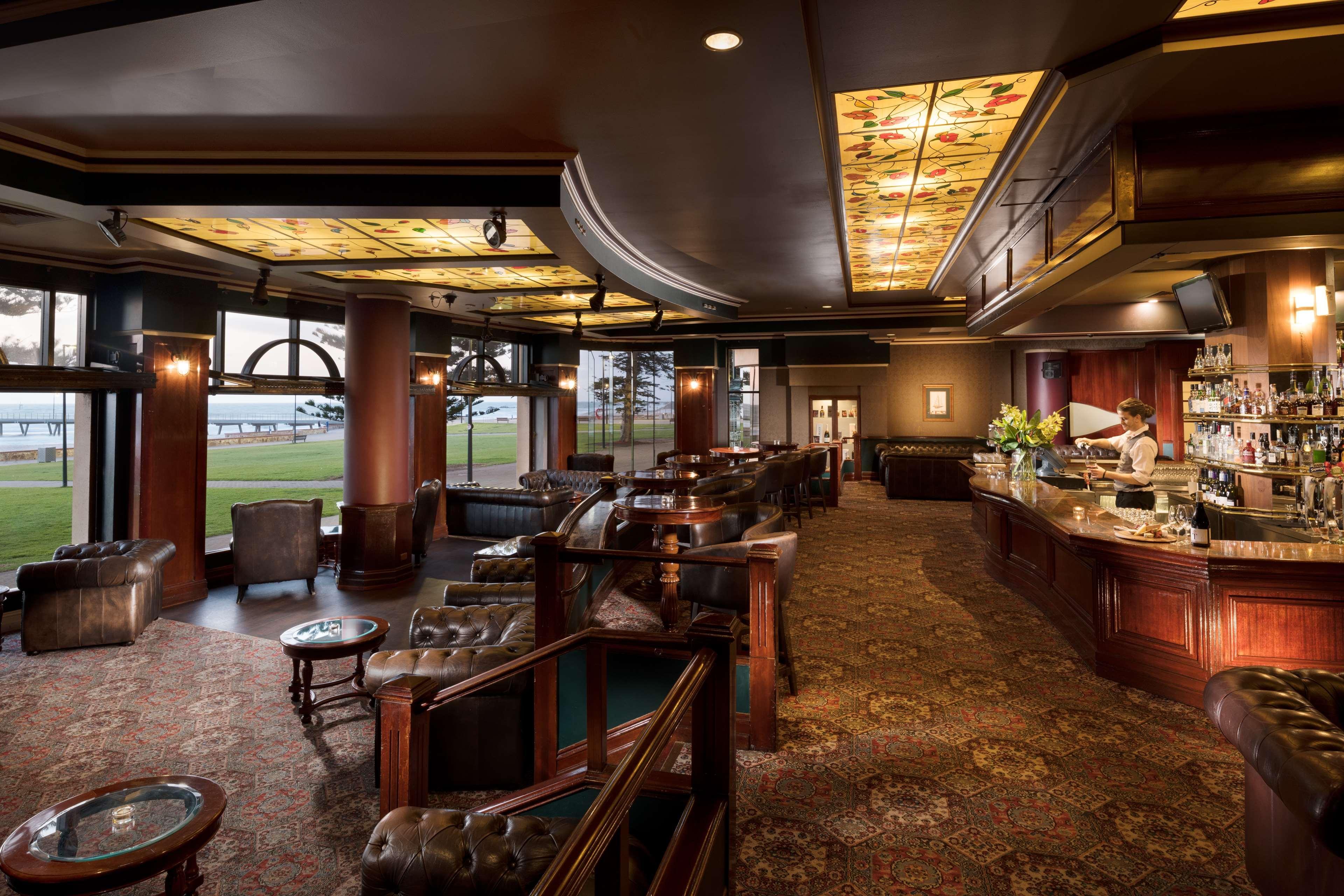 Stamford Grand Adelaide Hotel Glenelg Kültér fotó The photo depicts a stylish and upscale bar or lounge area. The interior features elegant wooden furniture, including plush chairs and tables. The ceiling is adorned with decorative elements, and the lighting provides a warm ambiance. A bar counter c