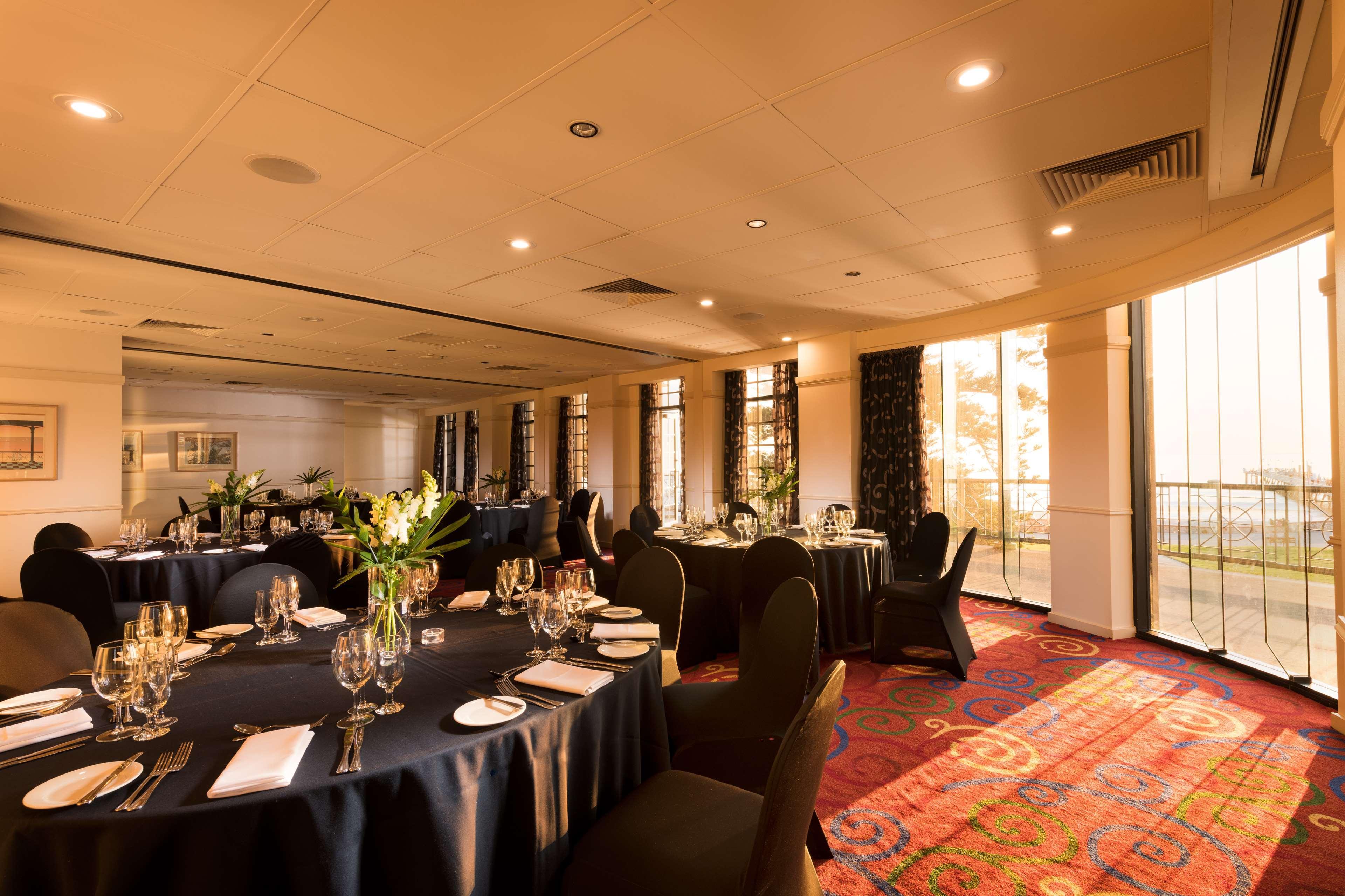 Stamford Grand Adelaide Hotel Glenelg Kültér fotó The photo shows a well-decorated event space or dining area. There are several round tables draped in dark tablecloths, each set with elegant dinnerware, including glasses and cutlery. The room features large windows that allow natural light to flood