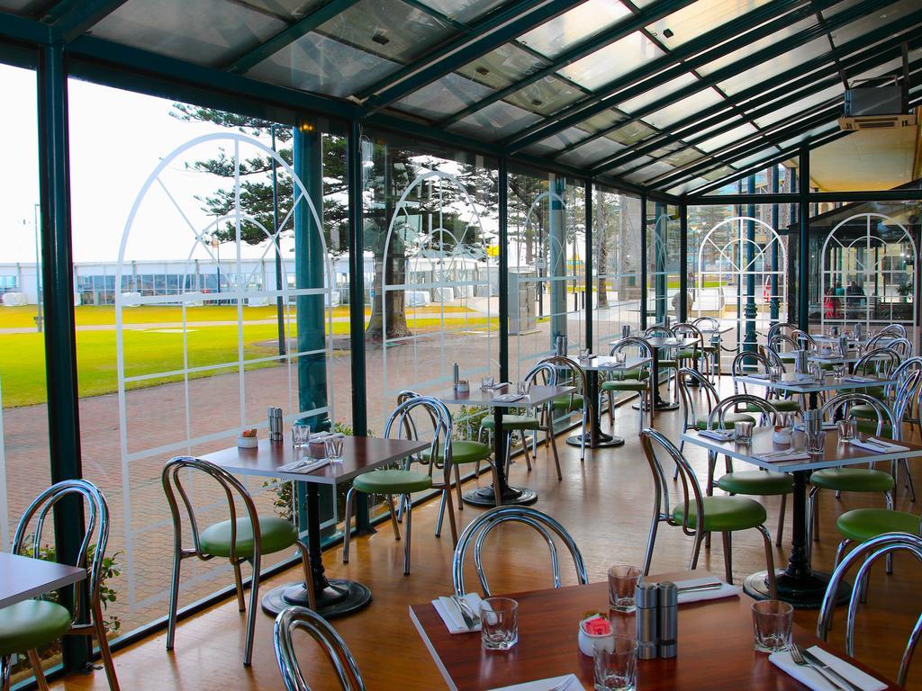 Stamford Grand Adelaide Hotel Glenelg Kültér fotó The photo shows the interior of a restaurant with a modern design. The space features several tables with green chairs, arranged in a way that allows for ample seating. Large glass windows provide a view of the outside, creating a bright and open atm