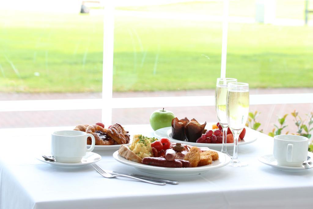 Stamford Grand Adelaide Hotel Glenelg Kültér fotó The photo displays a beautifully arranged breakfast setup on a white tablecloth. In the center, there is a large white plate with a variety of foods, including eggs, sausage, and fresh fruit. Surrounding the plate are a few other food items, such as 